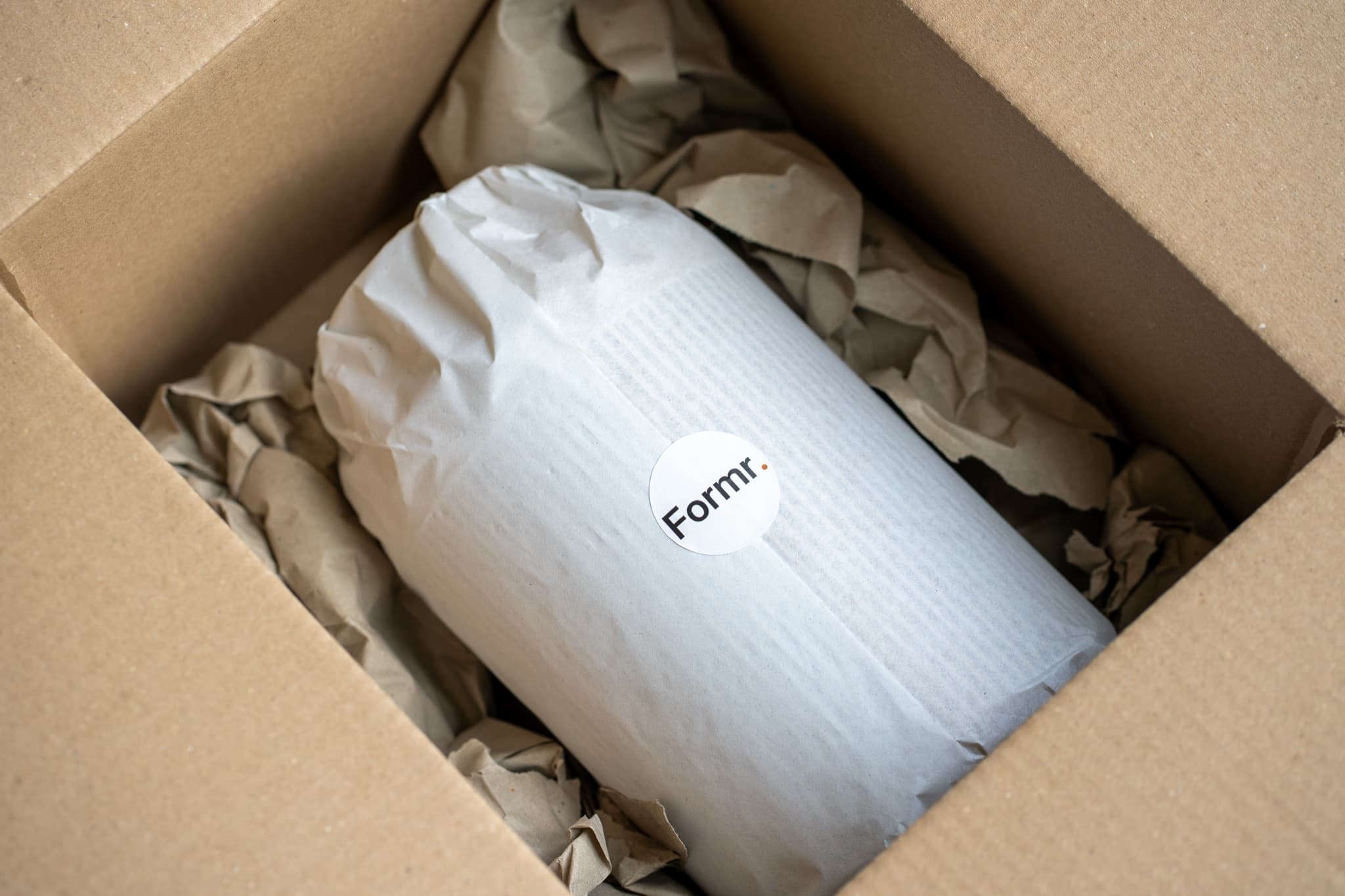 A print wrapped in tissue paper with a Formr sticker, in a cardboard box padded with kraft paper.